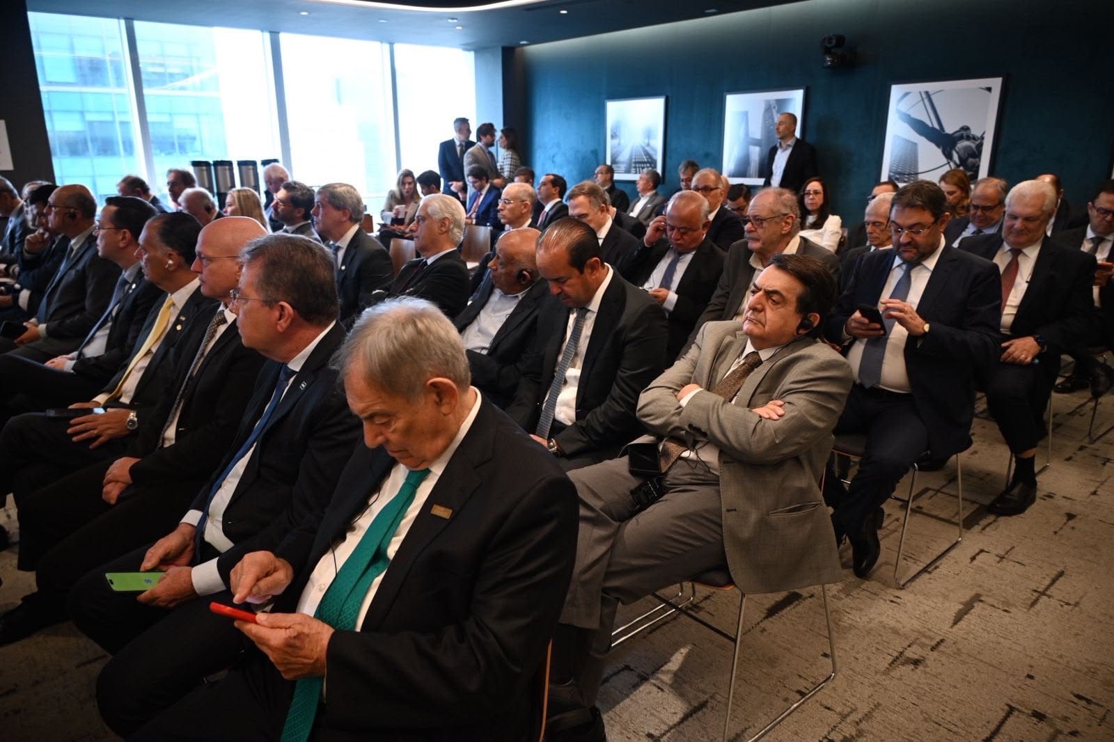 Público sentado em fileiras assistindo a apresentação, alguns com fones de tradução.