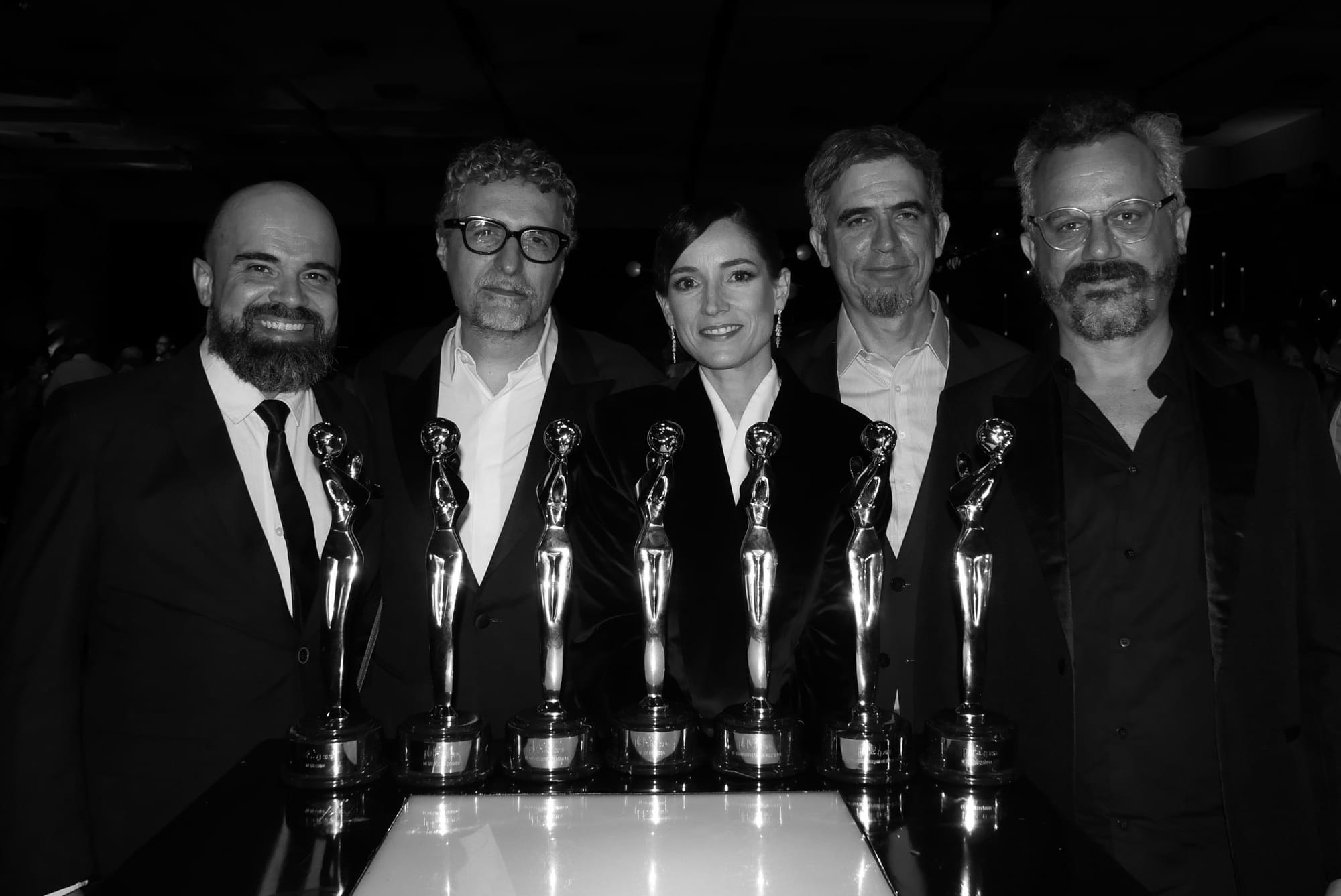 Equipe do filme posa com vários troféus do Prêmio Platino (foto em preto e branco)