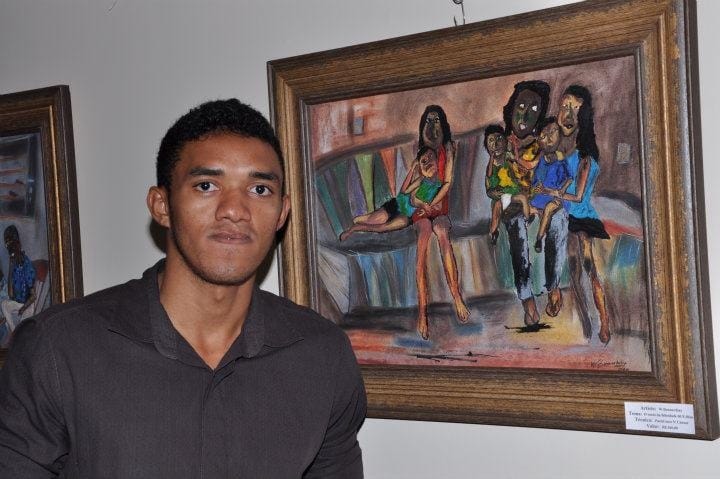 Retrato do artista W. Bonnardiny ao lado de uma de suas obras emolduradas na parede