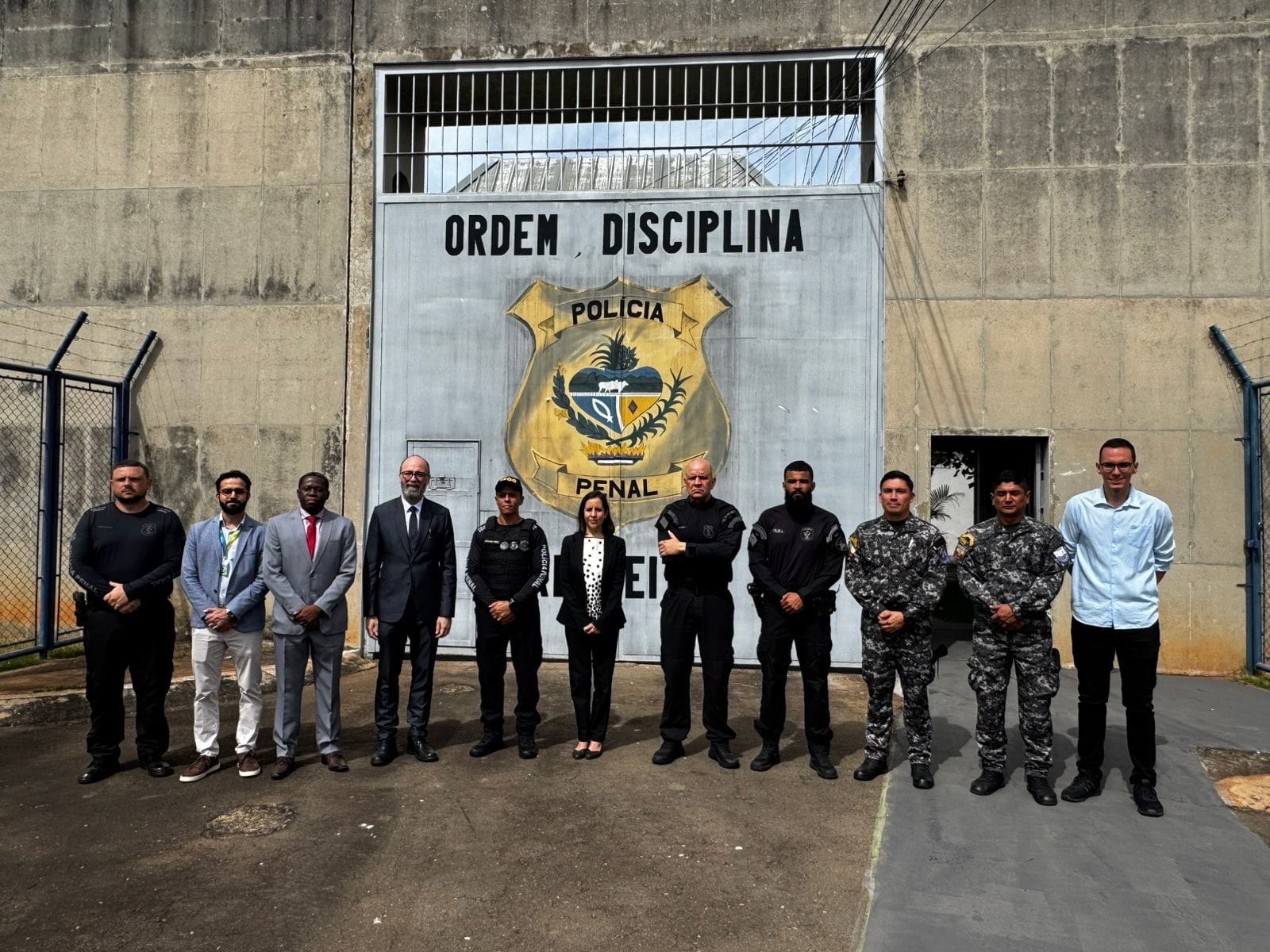 Portão com brasão Polícia Penal e grupo em frente