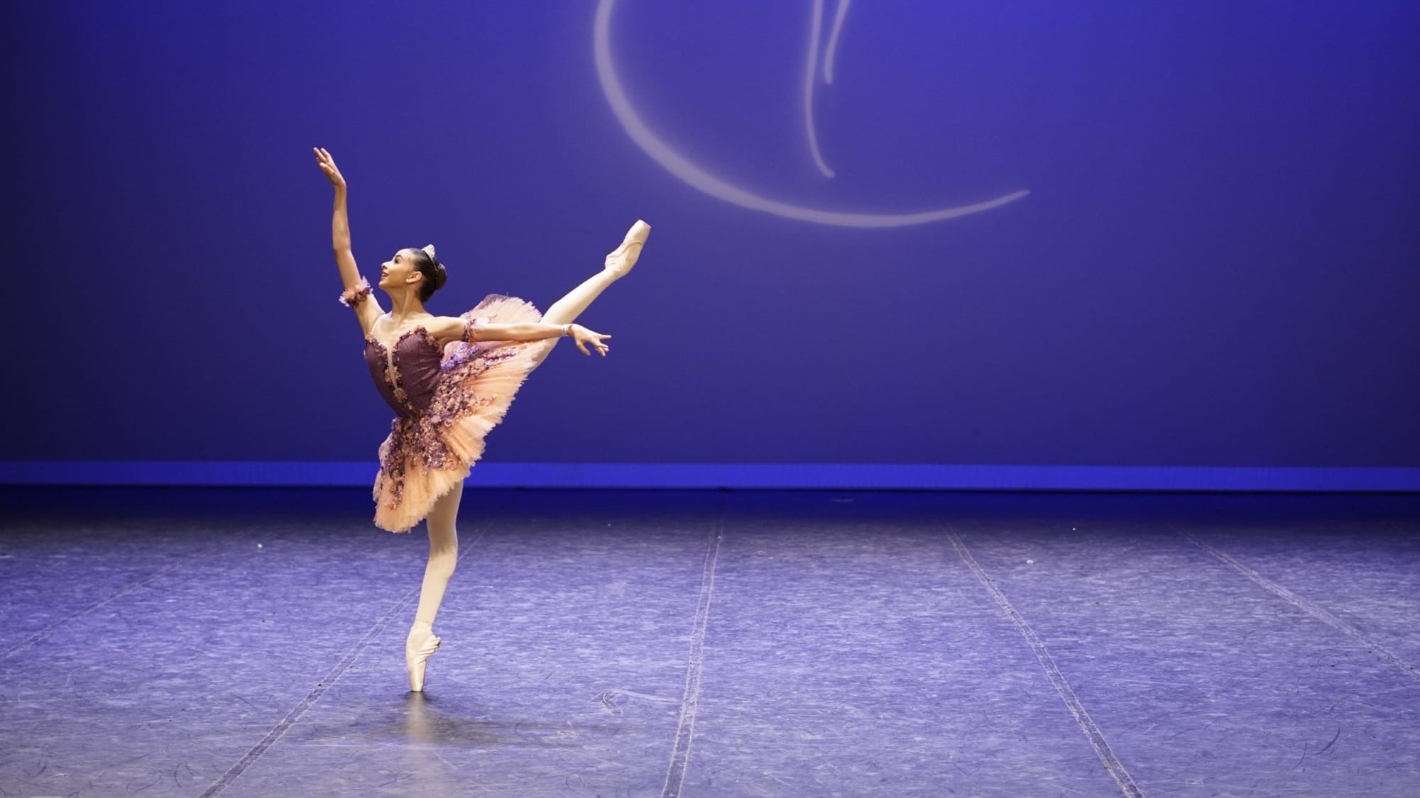 Bailarina em arabesque com figurino rosa e fundo azul