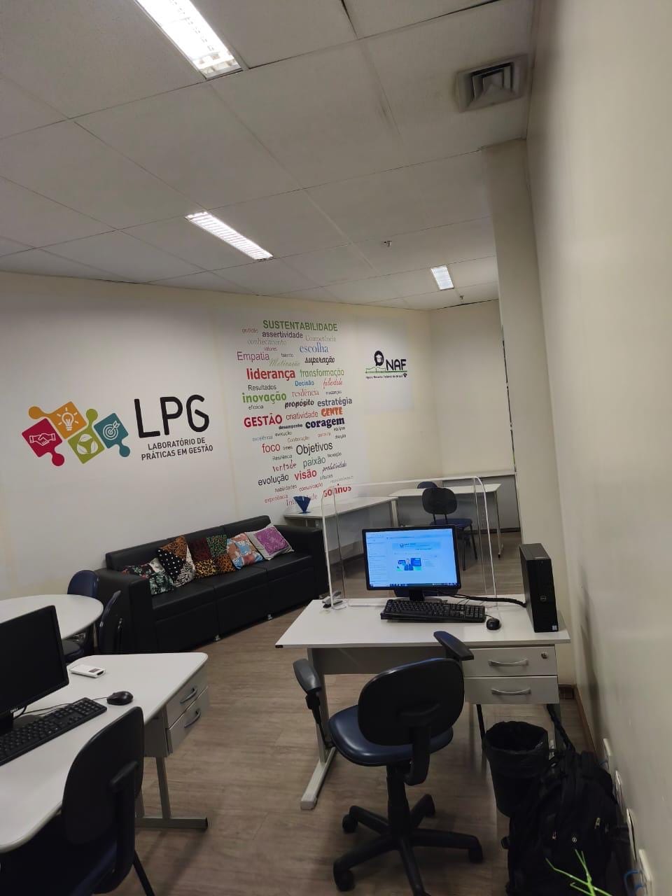 Computador e mesas na sala do NAF com logotipos do LPG e NAF na parede
