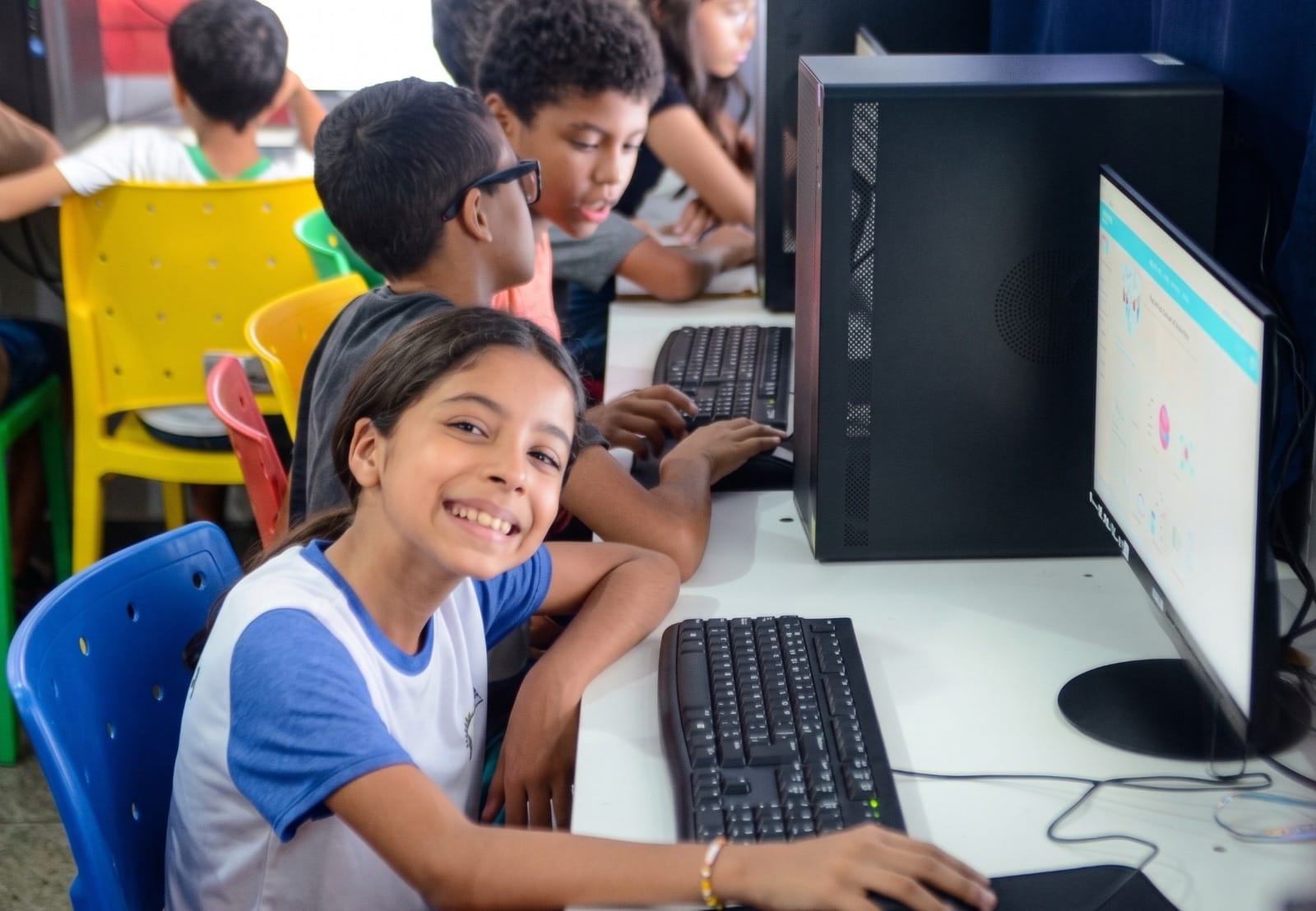 Alunos sorrindo e trabalhando em computadores em laboratório do Start