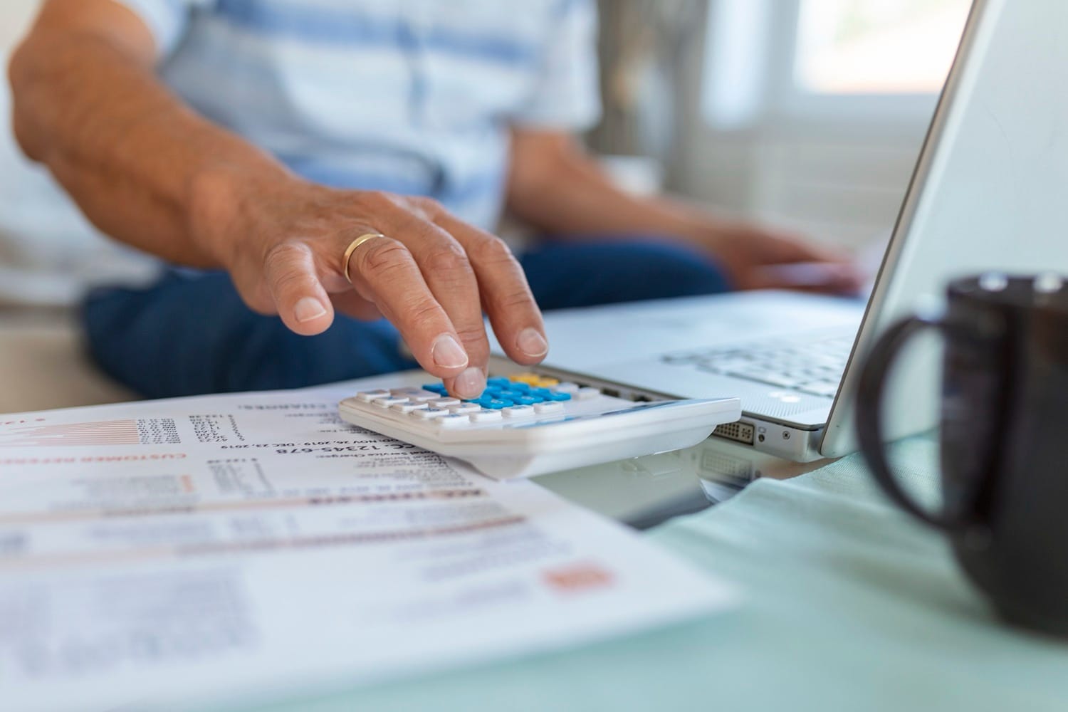 Mãos de idoso usando calculadora sobre mesa com documentos