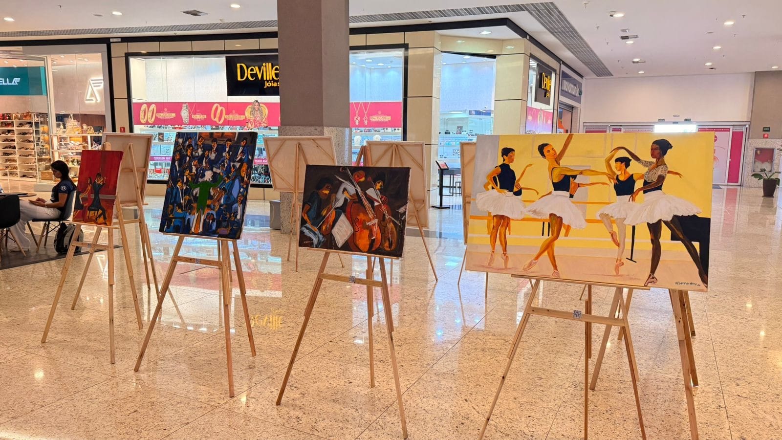 Várias telas em cavaletes alinhadas no espaço de exposição do shopping