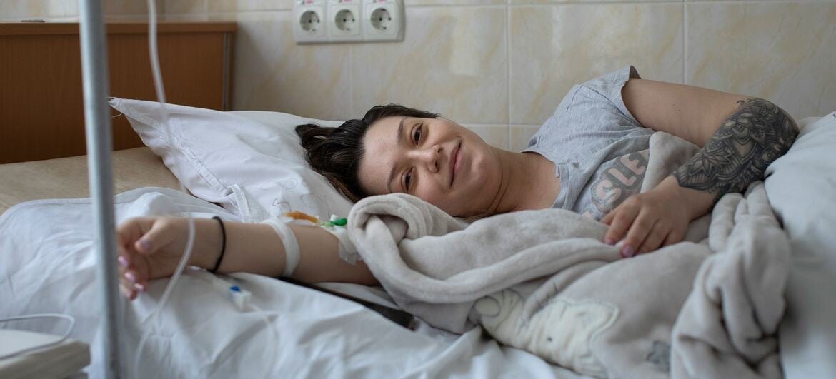 Paciente sorrindo deitado em leito hospitalar, com acesso venoso visível
