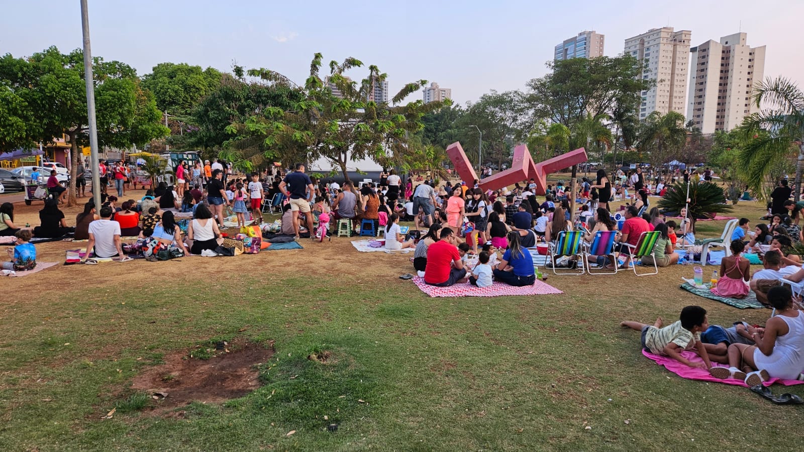 Público sentado em mantas no parque assistindo a tela inflável de cinema ao ar livre