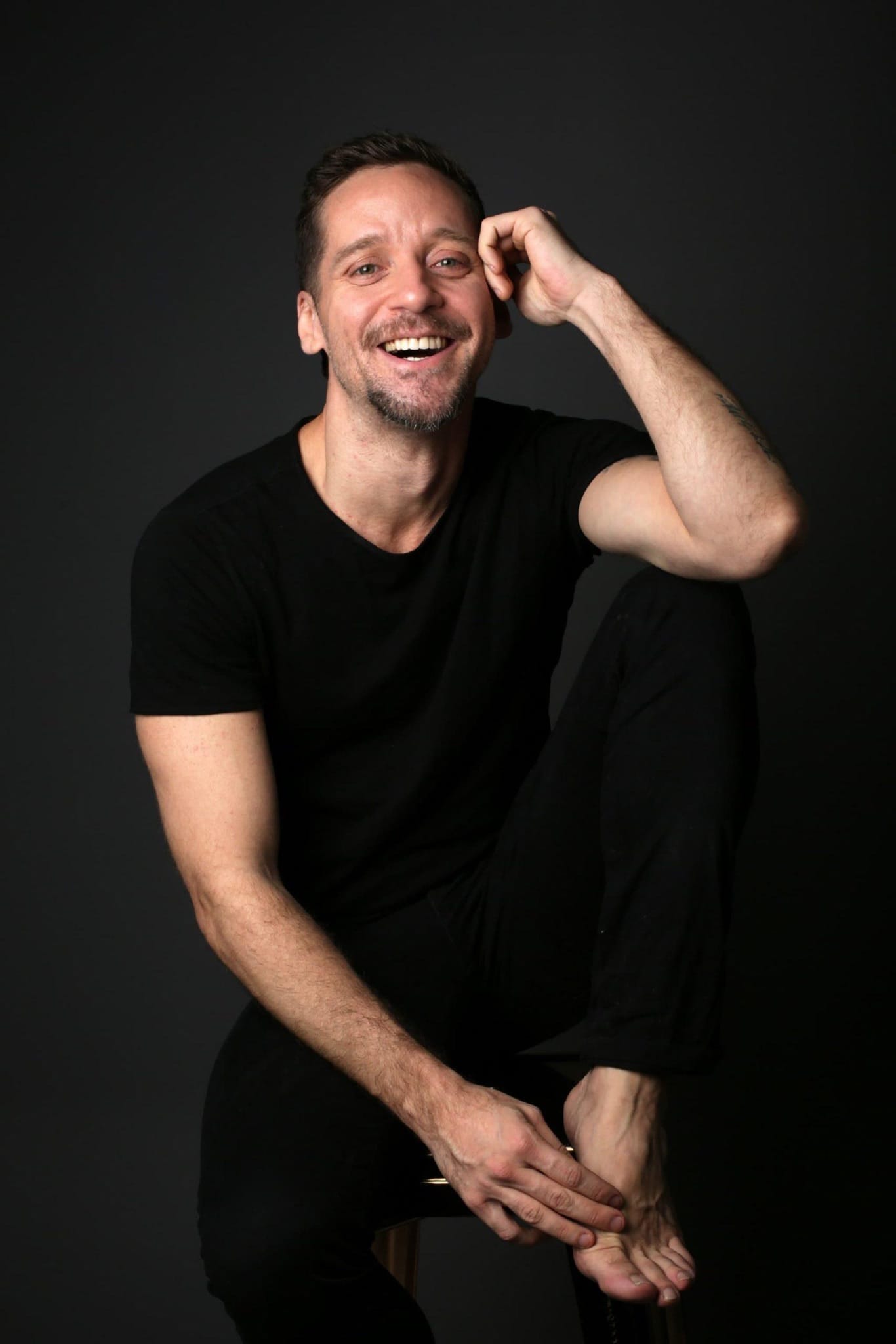 Retrato de Thiago Chagas sorrindo em fundo escuro