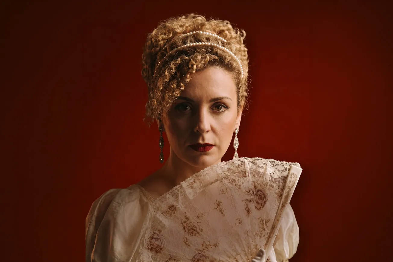 Retrato promocional de Ludmilla Bauerfeldt caracterizada como Violetta para a montagem de La Traviata, fundo vermelho.