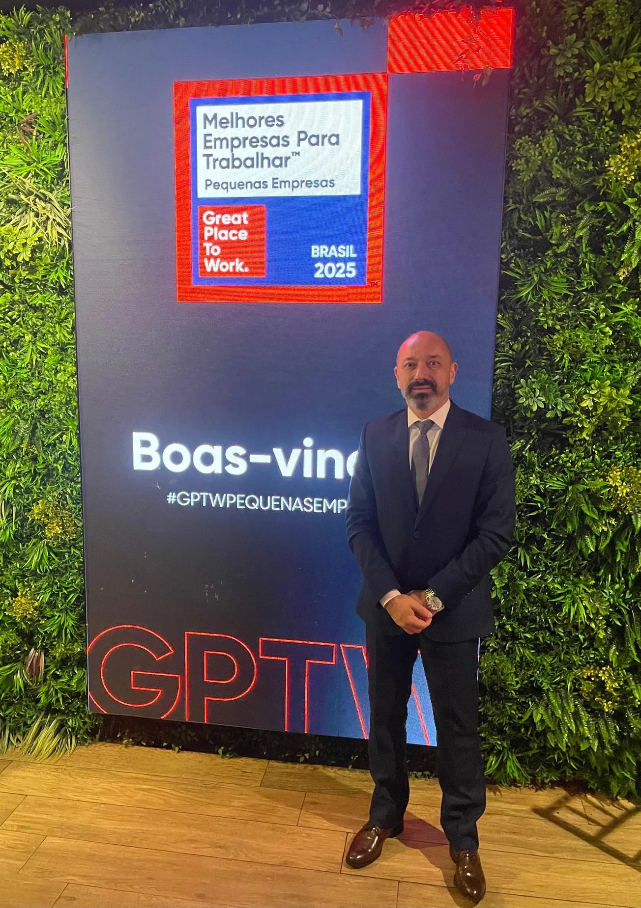Homem de terno posando ao lado de painel do evento Great Place To Work 2025