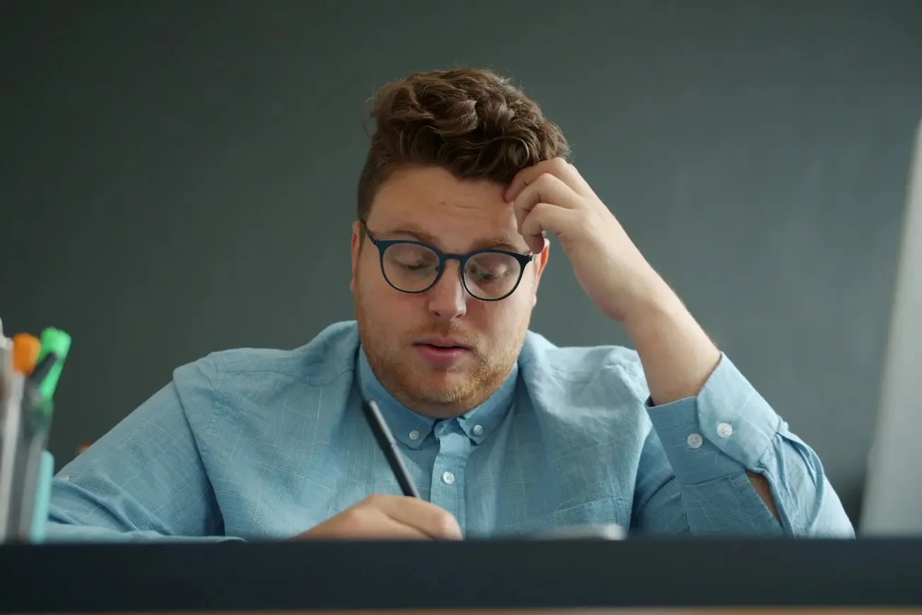 Homem com expressão preocupada escrevendo, ilustrando dúvida e ansiedade associadas à síndrome do impostor