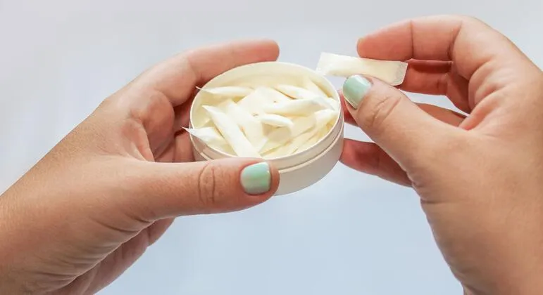 Mãos segurando pote com pouches de nicotina em sachês