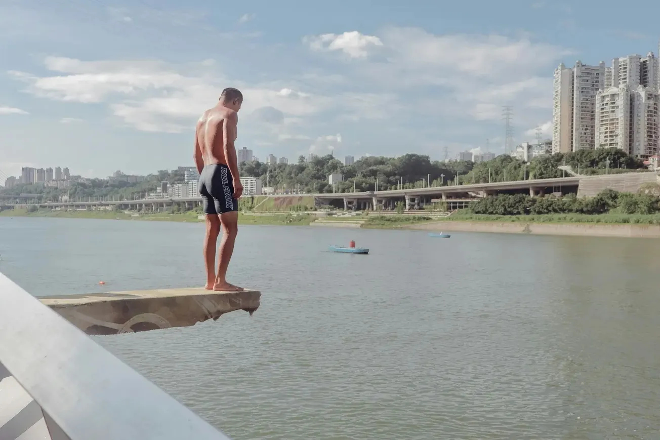 Homem em plataforma olhando para o rio com prédios ao fundo