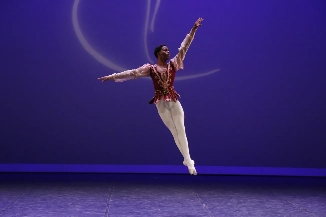 Bailarino em salto no palco com fundo azul durante apresentação